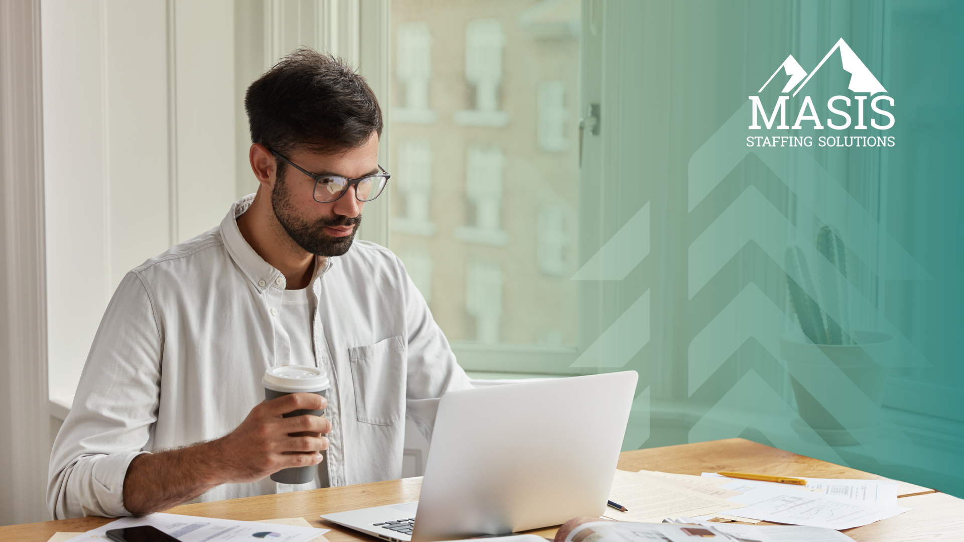 Employee sitting at a table with laptop, books, and papers, with coffee cup in hand