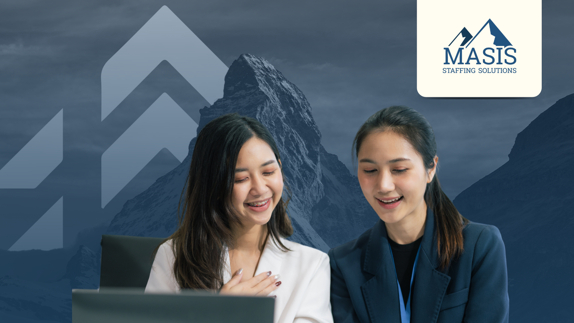 Two employees smile down at an office desk