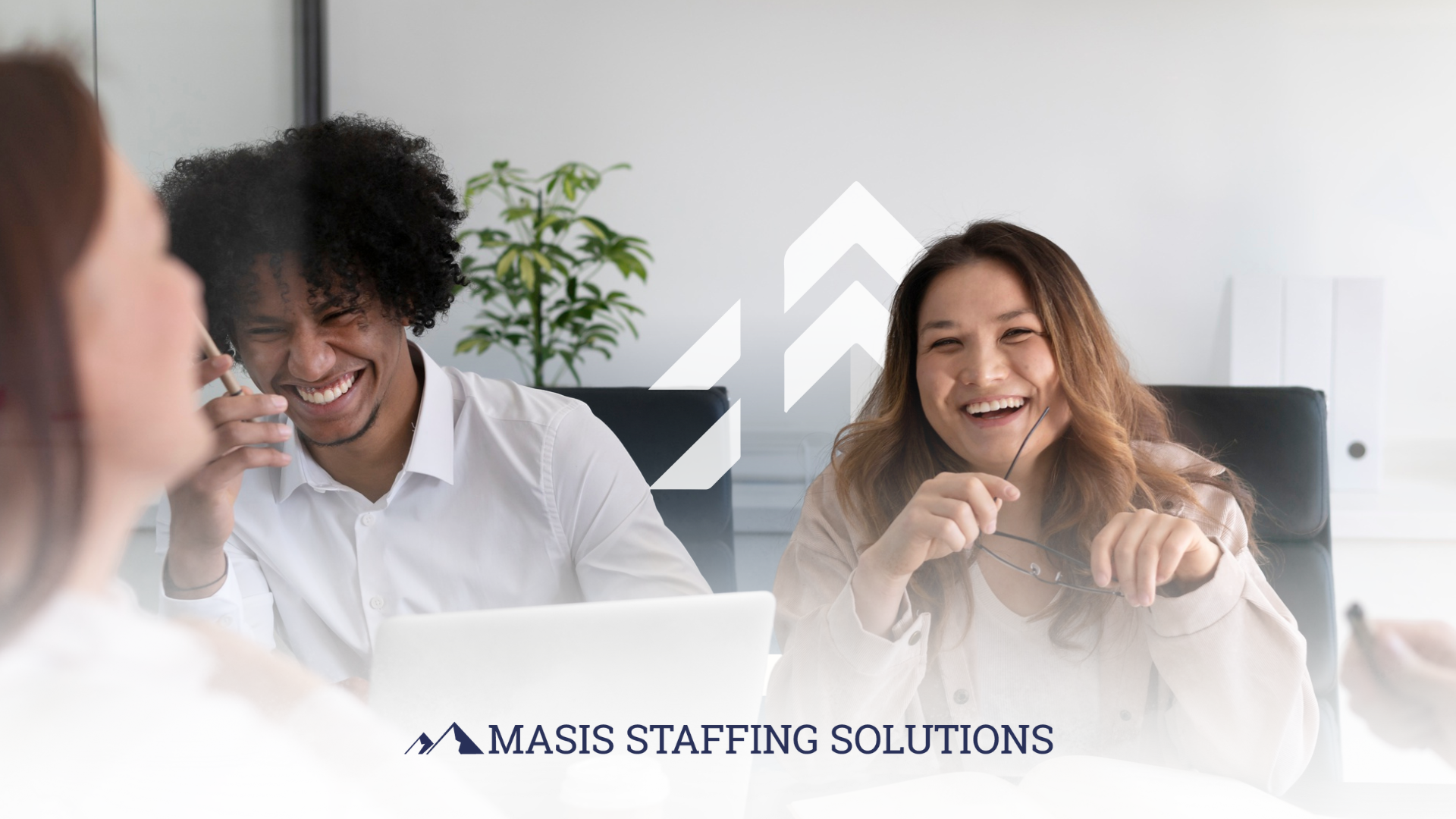 Employees at work laugh while meeting around a conference table