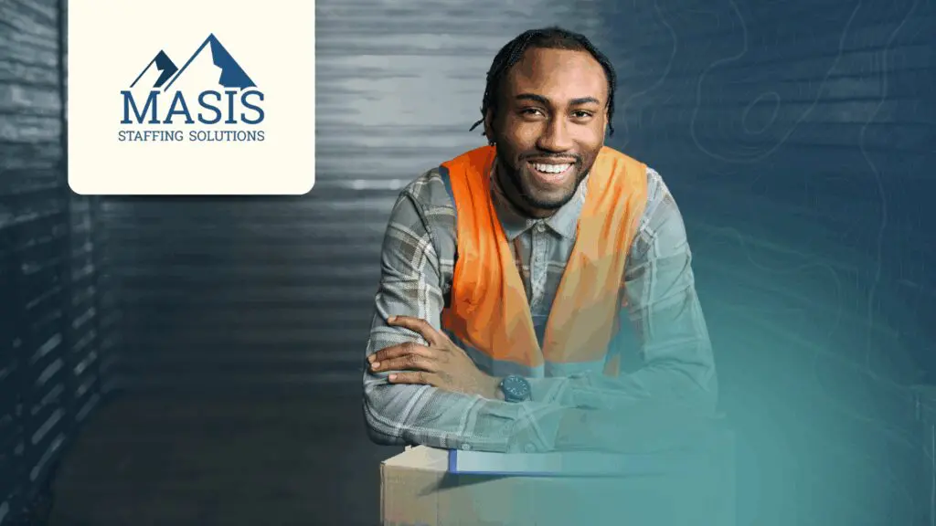 Employee in logistics and distribution leans on a box with a clipboard, wearing a safety vest
