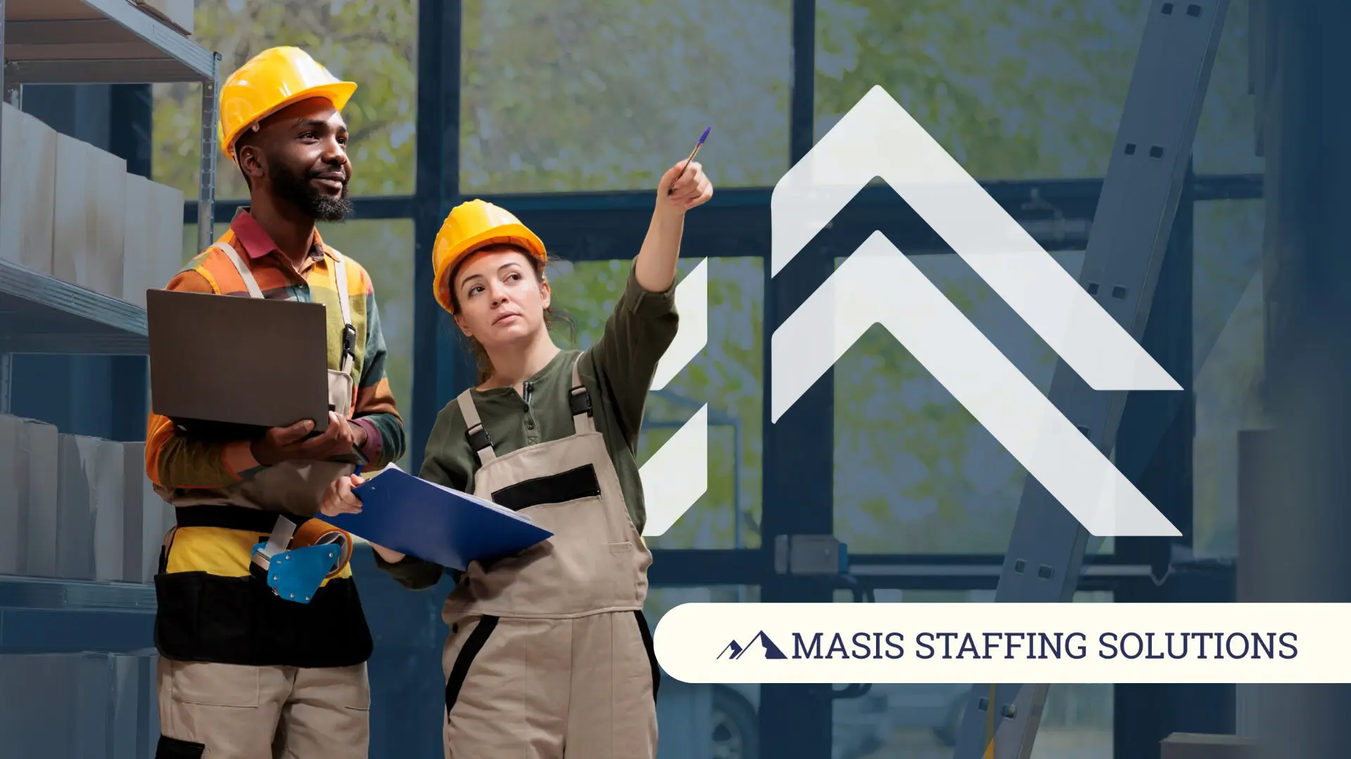 Two warehouse professionals work together wearing safety gear and holding a laptop and clipboard