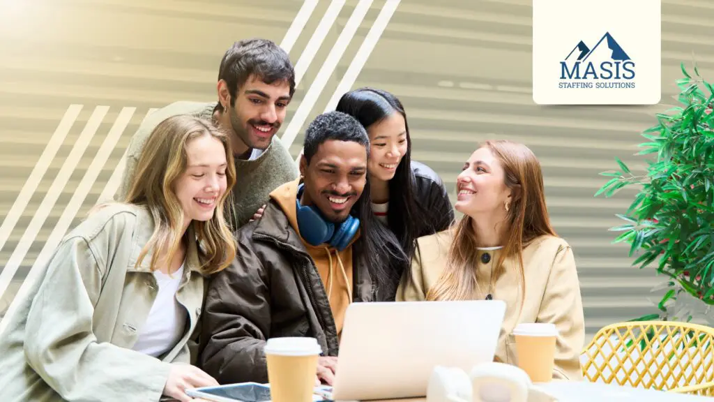 A group of Gen Z fresh graduates gather around a laptop