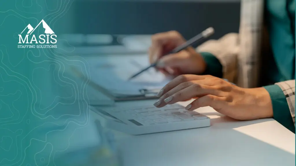A professional takes notes while using a calculator at a desk, representing the focus and preparation it takes to make a strong impression in a new temp role.