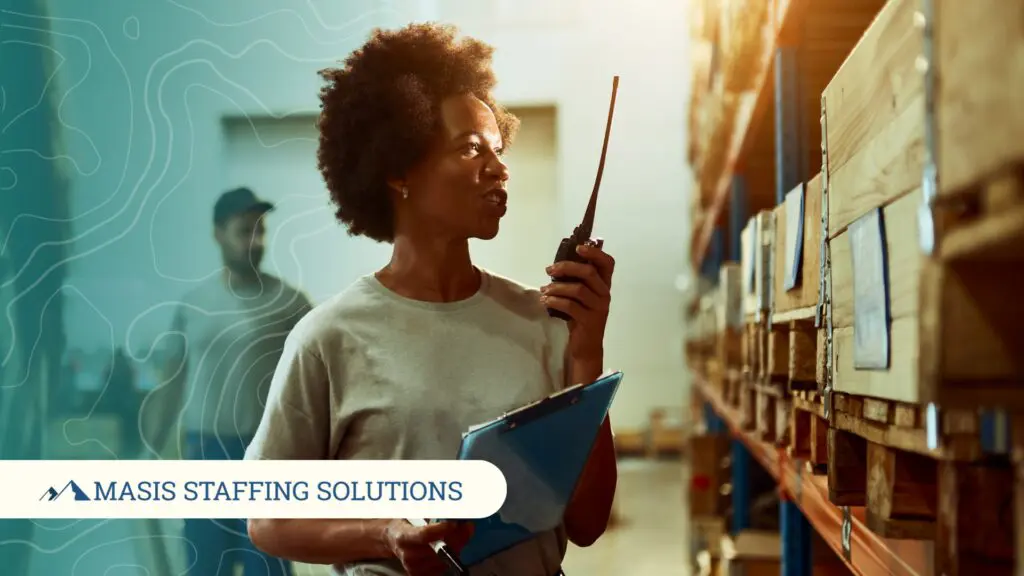 A woman in a warehouse uses a radio to coordinate with her team, illustrating the value of ongoing communication between employers and staffing partners.