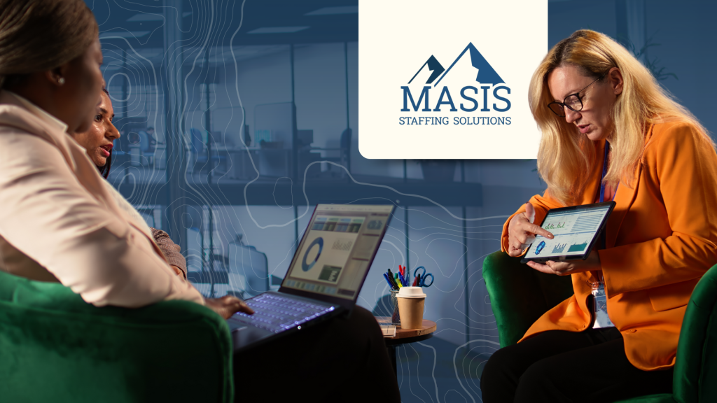 Woman in corporate attire shows a tablet displaying graphs and statistics to coworkers