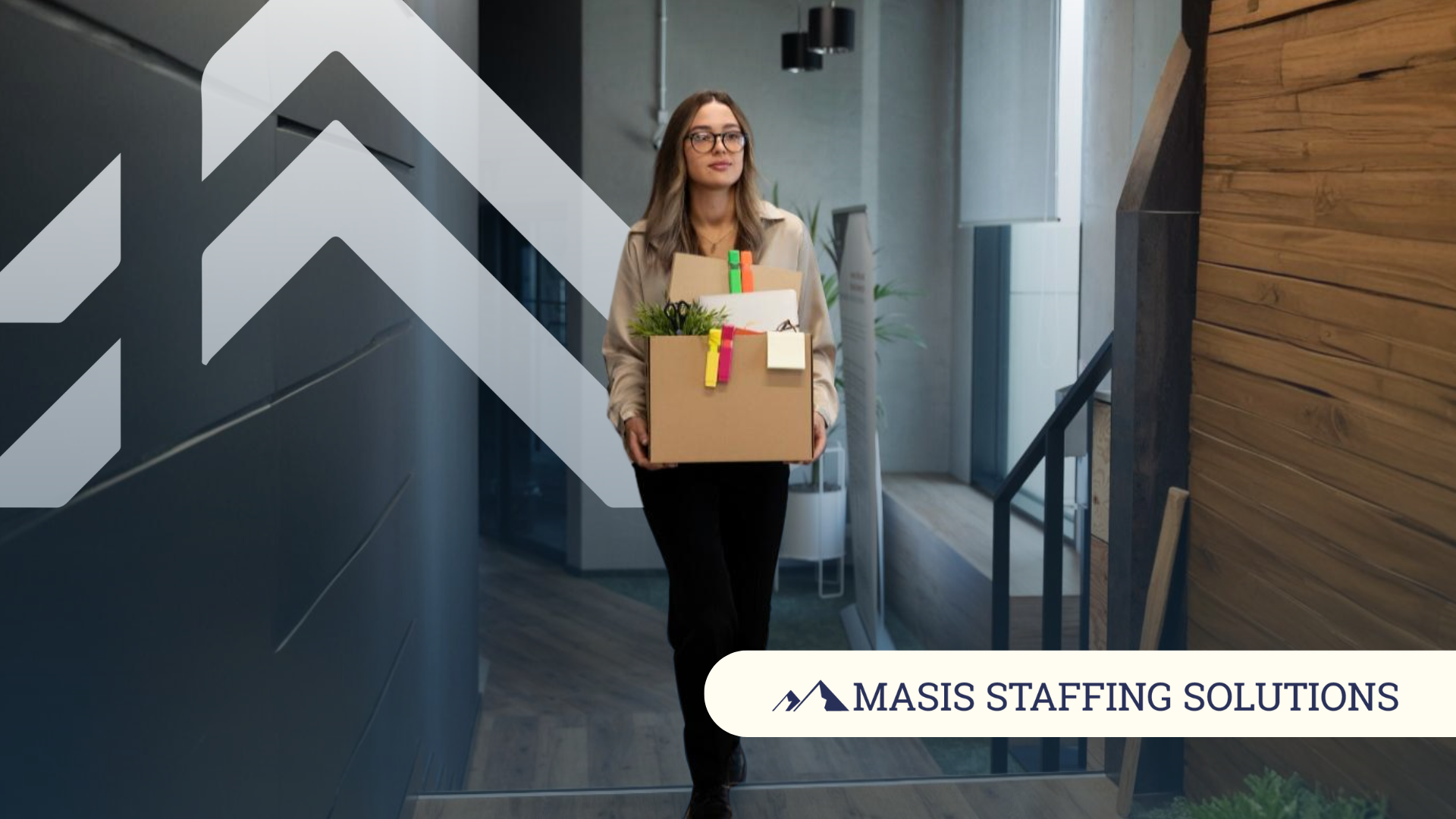 Female tech employee in corporate attire walks down an office hallway carrying a small box of personal items