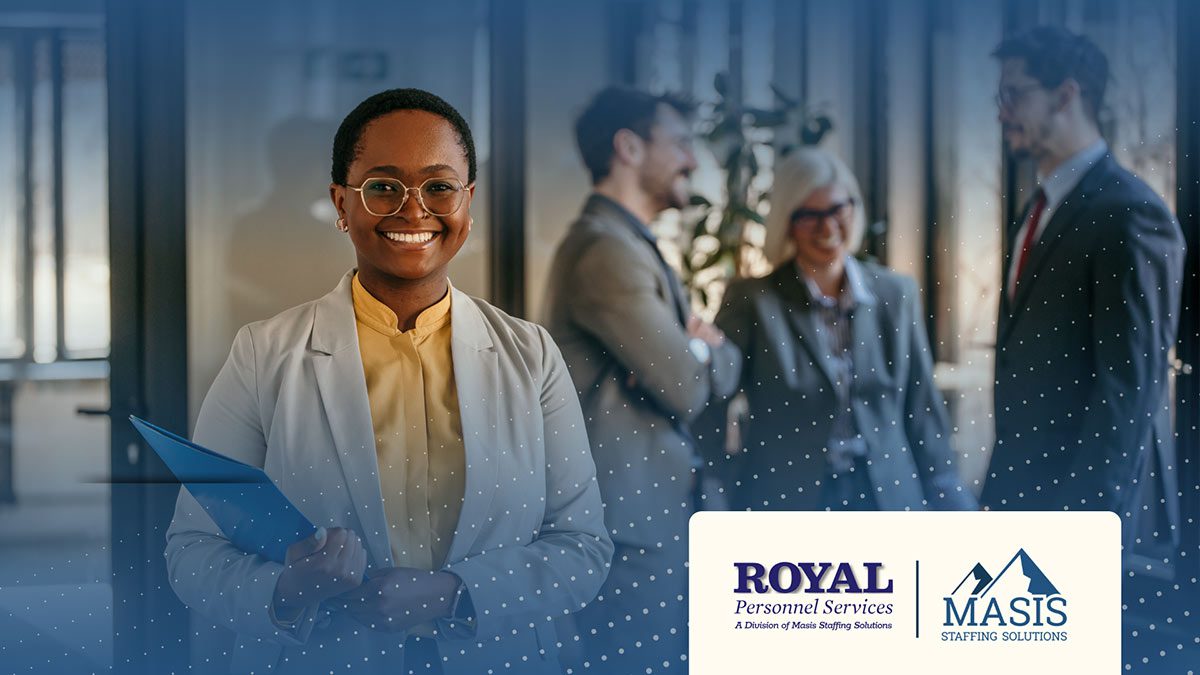 A smiling professional woman in a light gray blazer holds a blue folder in a modern office, with three colleagues in business attire talking in the background. The Royal Personnel Services and Masis Staffing Solutions logos appear in the bottom right corner.